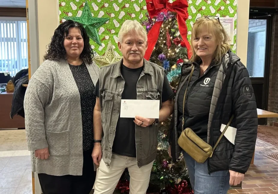 Three people with envelope by Christmas tree
